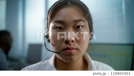 Close up portrait of Asian woman in headset working in call center office 119803401