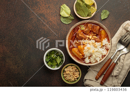 Delicious massaman curry with beef, potatoes, rice, and peanuts is served in bowl top view, Thai cuisine, space for text 119803436