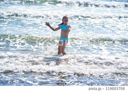 An 8 year old girl in a swimsuit having fun in the sea waves. An 8 year old girl in a swimsuit having fun in the sea waves. 119803708