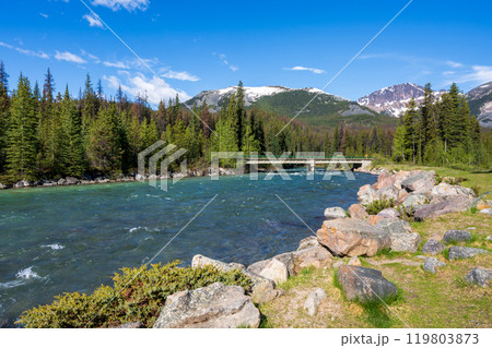 A cement bridge over a river in forest against blue sky and a mountain in the background. Maligne River in Jasper National Park, Alberta, Canada. Canadian Rockies. A cement bridge over a river in forest against blue sky and a mountain in the background. Maligne River in Jasper National Park, Alberta, Canada. Canadian Rockies. 119803873