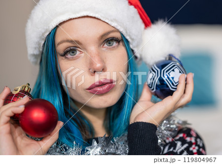 Portrait of a beautiful hipster Caucasian woman in Christmas clothes.She poses looking at the camera holding colorful balls and a silver decoration around her neck.Beauty,Christmas holidays,positivity 119804967