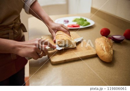 Person slicing fresh baguette on a kitchen countertop Person slicing fresh baguette on a kitchen countertop 119806061