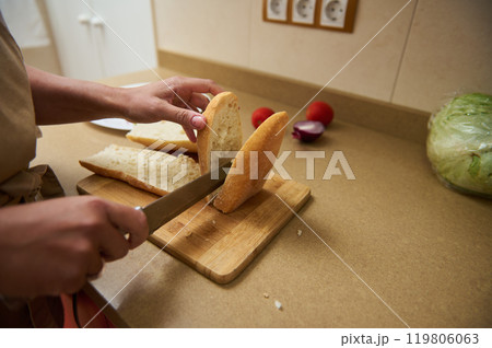 Person slicing fresh bread on a wooden cutting board in kitchen Person slicing fresh bread on a wooden cutting board in kitchen 119806063