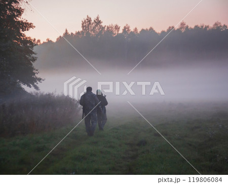Men in camouflage with weapons move on an autumn morning along edge of field and forest. Men in camouflage with weapons move on an autumn morning along edge of field and forest. 119806084