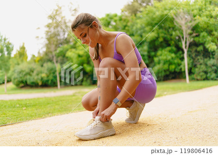An Active Woman is Skillfully Tying Her Shoelaces While Enjoying the Park Environment 119806416