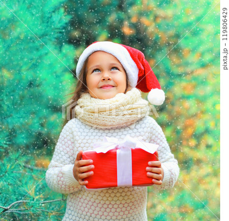 Christmas child little girl in santa red hat with gift box dreaming near a tree 119806429