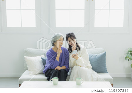 リビングでスマホを見るシニア女性と若い女性　　　　 119807855