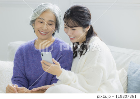 リビングでスマホを見るシニア女性と若い女性 リビングでスマホを見るシニア女性と若い女性 119807861