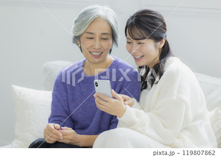 リビングでスマホを見るシニア女性と若い女性　　　　 119807862