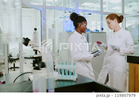 Scientists engaging in lab work, examining samples on slide. Laboratory equipment and intricate procedures evident in workspace 119807979