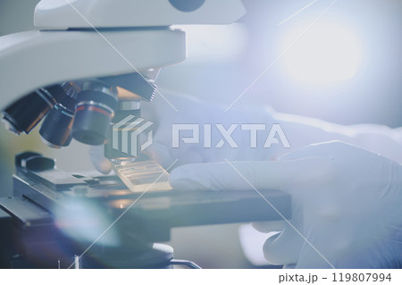 Gloved hand adjusting settings on microscope for scientific research in laboratory environment, ensuring precision and accuracy Gloved hand adjusting settings on microscope for scientific research in laboratory environment, ensuring precision and accuracy 119807994