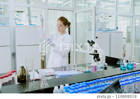 Scientist in white lab coat conducting experiments in advanced laboratory setup with various scientific equipment and glassware Scientist in white lab coat conducting experiments in advanced laboratory setup with various scientific equipment and glassware 119808019