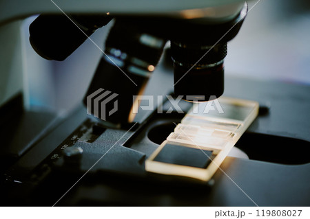 Microscope slide placed under the lenses of a laboratory microscope showing detailed components and parts. Image captures intricate details within a scientific research setting Microscope slide placed under the lenses of a laboratory microscope showing detailed components and parts. Image captures intricate details within a scientific research setting 119808027