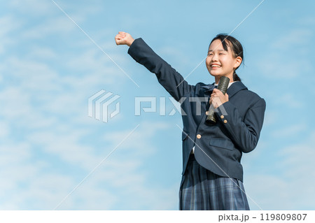 青空の下で卒業証書の丸筒を持ってガッツポーズする卒業生の女子中学生 119809807