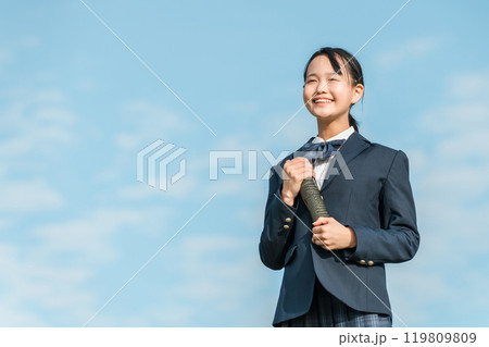 青空の下で卒業証書の丸筒を持つ卒業生の女子中学生 119809809