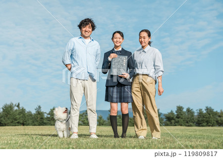青空の下で卒業証書を持つ笑顔の娘と両親・ファミリー 119809817