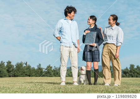 青空の下で卒業証書を持つ笑顔の娘と両親・ファミリー 119809820