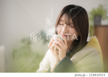 冬のリビングで温かい飲み物を飲むくつろぐ若い女性のクローズアップ 冬のリビングで温かい飲み物を飲むくつろぐ若い女性のクローズアップ 119810553