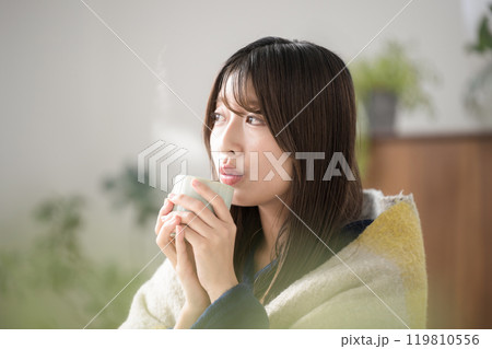 冬のリビングで温かい飲み物を飲むくつろぐ若い女性のクローズアップ　熱い飲み物を冷ます横顔 119810556