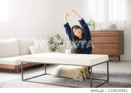 部屋に座って伸びをする若い女性　遅く起きた冬の朝のリラックス 119810561