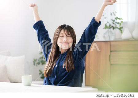 部屋に座って伸びをする若い女性　秋冬の朝のリラックスのパジャマの上半身 119810562