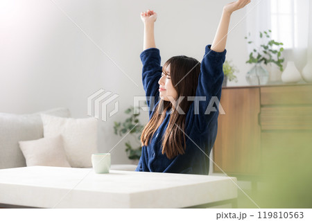 部屋に座って伸びをする若い女性　秋冬の朝のリラックスのパジャマの上半身 119810563