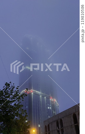 A high-rise building disappears in the evening fog A high-rise building disappears in the evening fog 119810586