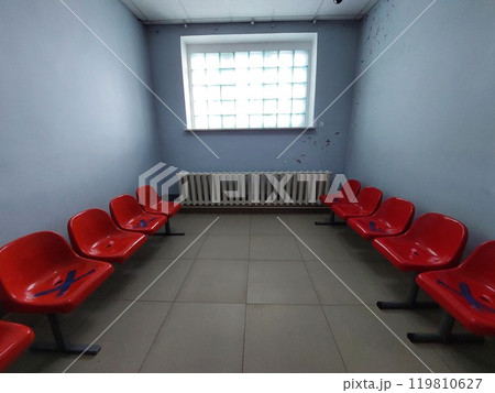 A gloomy corridor with an opaque window and cracked walls, a radiator and red armchairs A gloomy corridor with an opaque window and cracked walls, a radiator and red armchairs 119810627