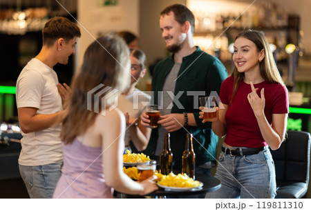 Happy mens and womens drinking beer and eating crisps, laughing and spending time together in bar 119811310