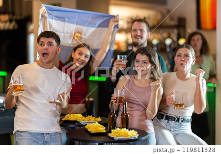 Group of emotional Argentine fans with the national flag watch the match on TV with interest and actively comment 119811328