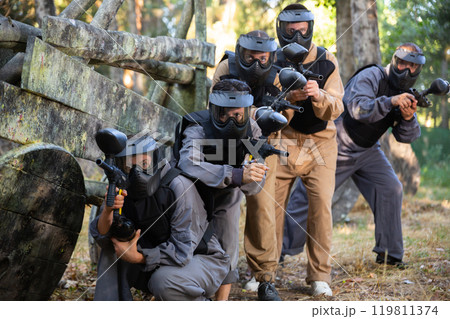 Group of paintball players aiming and shooting with guns outdoors 119811374