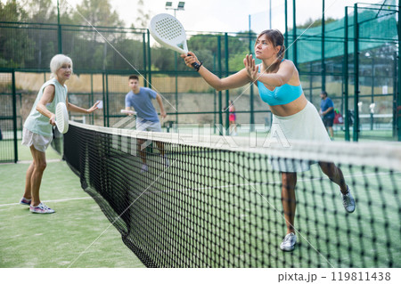 Happy woman learning to play padel game on tennis court outdoor. Other athletes are training in background 119811438