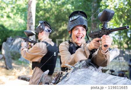 Woman fires a gun with passion while playing paintball Woman fires a gun with passion while playing paintball 119811685