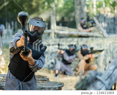Paintball player in protective uniform aiming and shooting with guns 119811869