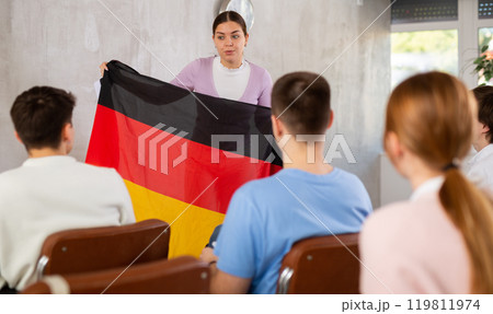 Young woman teacher holding flag of Germany in front of group of students 119811974