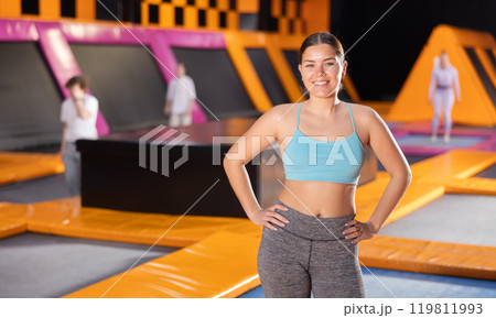 Portrait of cheerful young female in sportswear posing and smiling at camera on colorful trampoline in game club 119811993