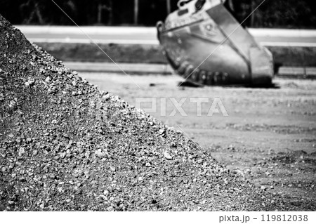 Aggregate dirt pile at a construction site with a defocused excavator bucket in the background. Aggregate dirt pile at a construction site with a defocused excavator bucket in the background. 119812038