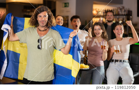 Company of sports fans waving flag of Sweden and supporting national team with beer in bar 119812050