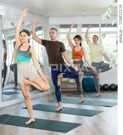 Woman in sportswear exercising with group active people during yoga class in modern fitness center, standing in 119812114