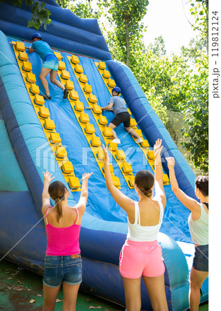 Two male friends climbing on inflatable slide with wooden poles 119812124