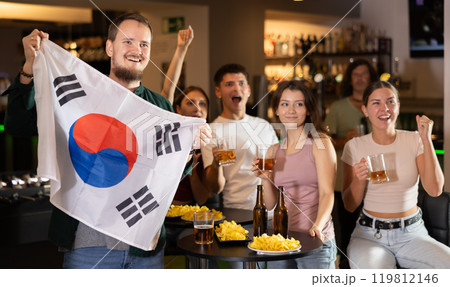 Football fans gesturing emotionally after goal scored by favorite team while watching championship match on TV in sports bar with North Korea flag 119812146
