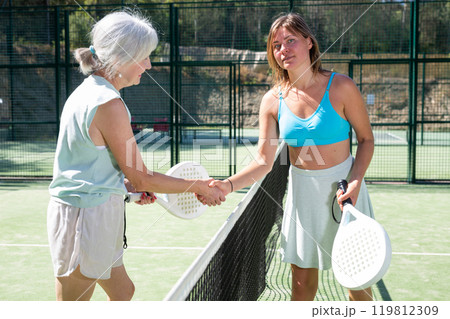 Senior and young women handshaking after padel tennis match Senior and young women handshaking after padel tennis match 119812309