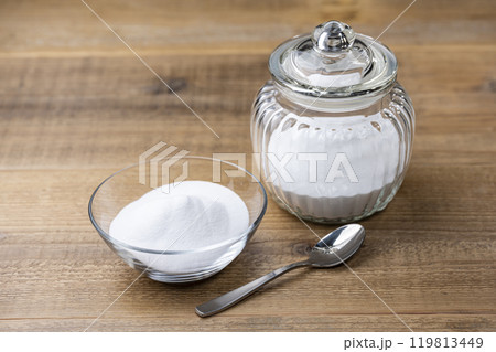 木目テーブルに並ぶガラス瓶とボウルに入った重曹の白い粉とスプーン 119813449