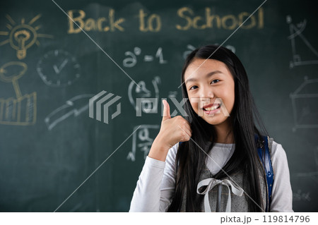 A girl is giving a thumbs up in front of a blackboard with the words Back to School written on it 119814796