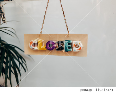 Multicolored creative sign, signboard hanging on a glass doors of a store, shop with the text Closed. A small business merchandise. Mode of operation. 119817374