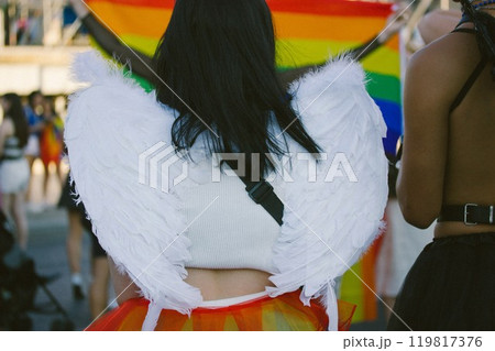Young girl in angel costume with white wings back view. People in costumes at carnival, gay parade in summer. Youth festival. Multicoloured gay pride  119817376