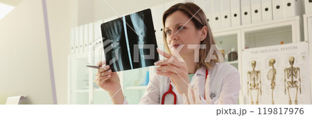 Doctor studies X-ray picture of patient arm sitting at desk Doctor studies X-ray picture of patient arm sitting at desk 119817976