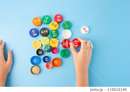 Teaching times tables to kids, ideas to make teaching multiplication fun. DIY, bottle caps with multiplication exercises on blue background, practice for kids 119818196