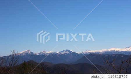 Snow-capped peaks and forested mountains of the Republic of Adygea against a clear blue sky, view from an observation deck of the North Caucasus mountain range 119818795