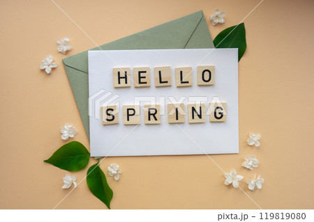HELLO SPRING text on Composition with envelope and beautiful spring lilac flowers on beige background.. Branches of lilac blooming bouquet HELLO SPRING text on Composition with envelope and beautiful spring lilac flowers on beige background.. Branches of lilac blooming bouquet 119819080